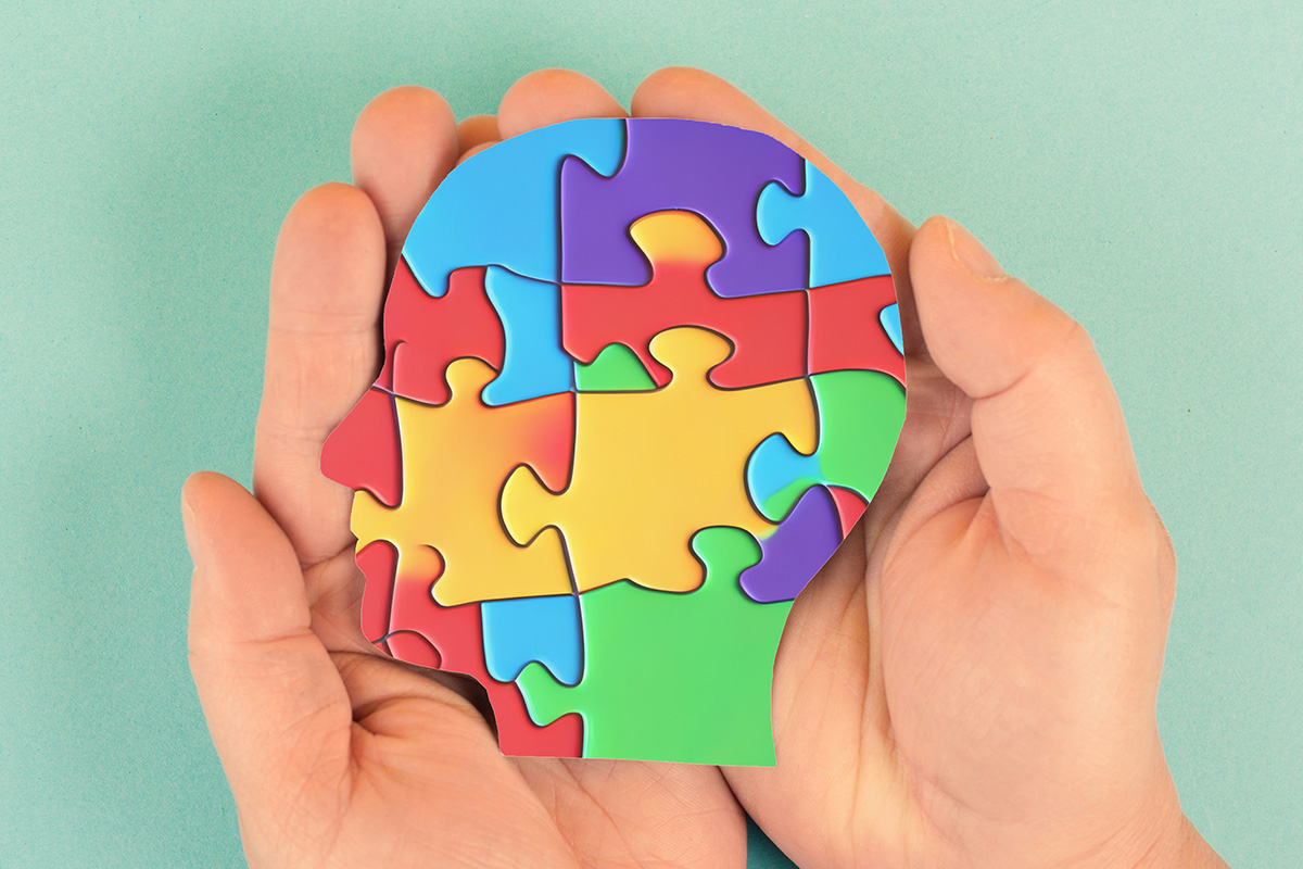 Two hands cupped together holding a multi-colored puzzle that is shaped like a human head