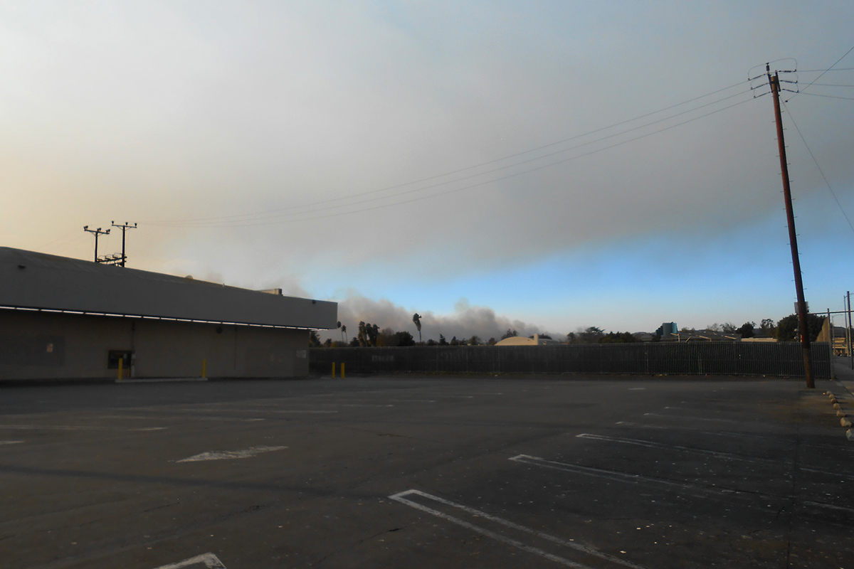 Clouds of smoke drift over an empty parking lot outside of a building.