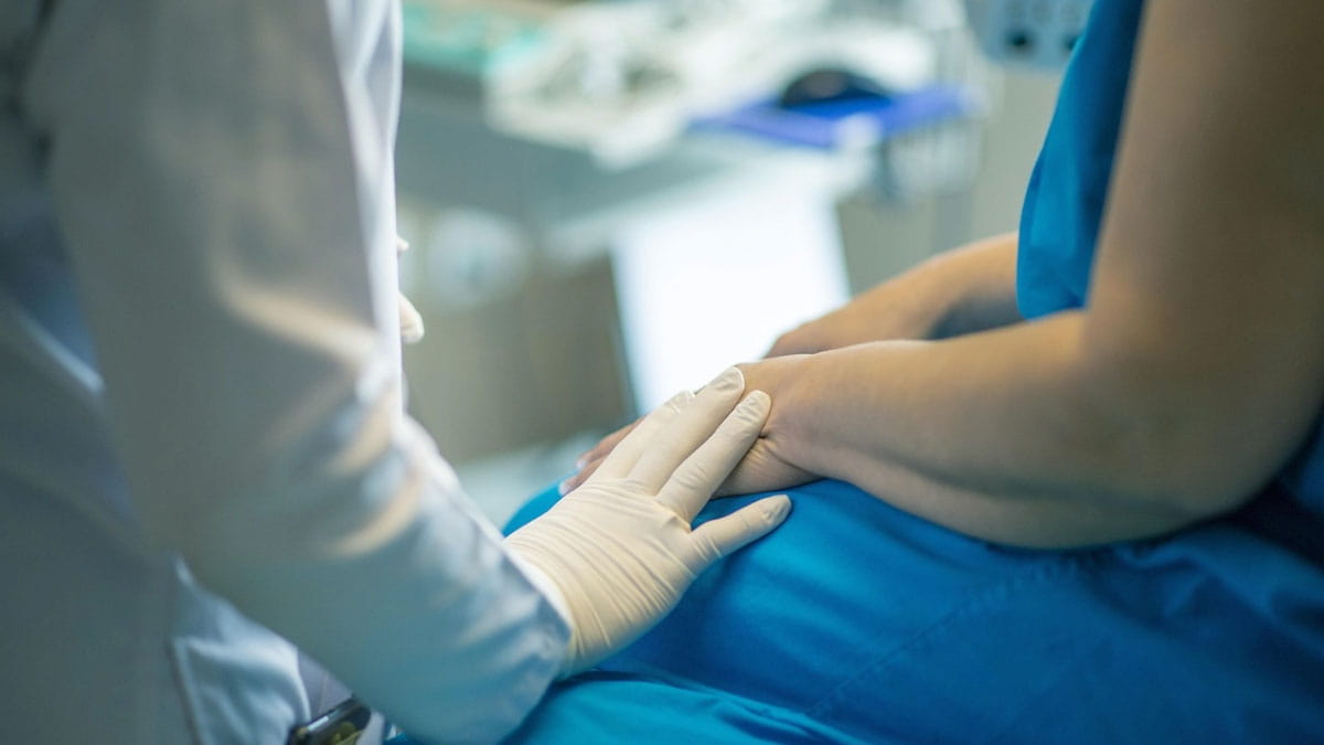 A doctor touches a patient's hand in an exam room