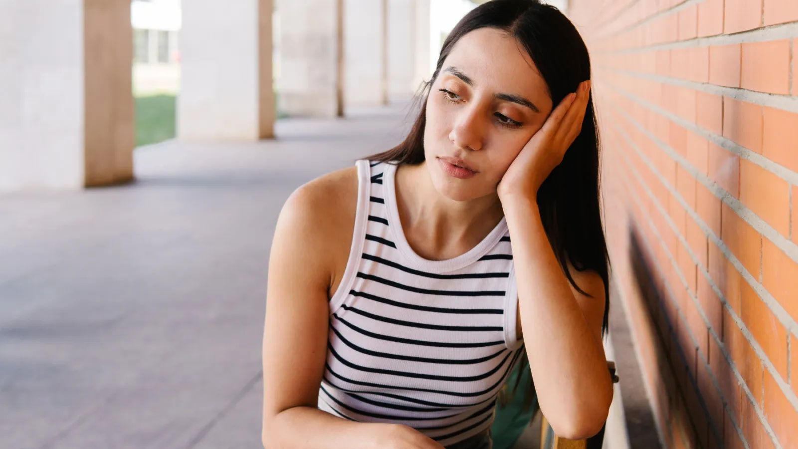 Woman in a striped tank top rests her head on her hand.