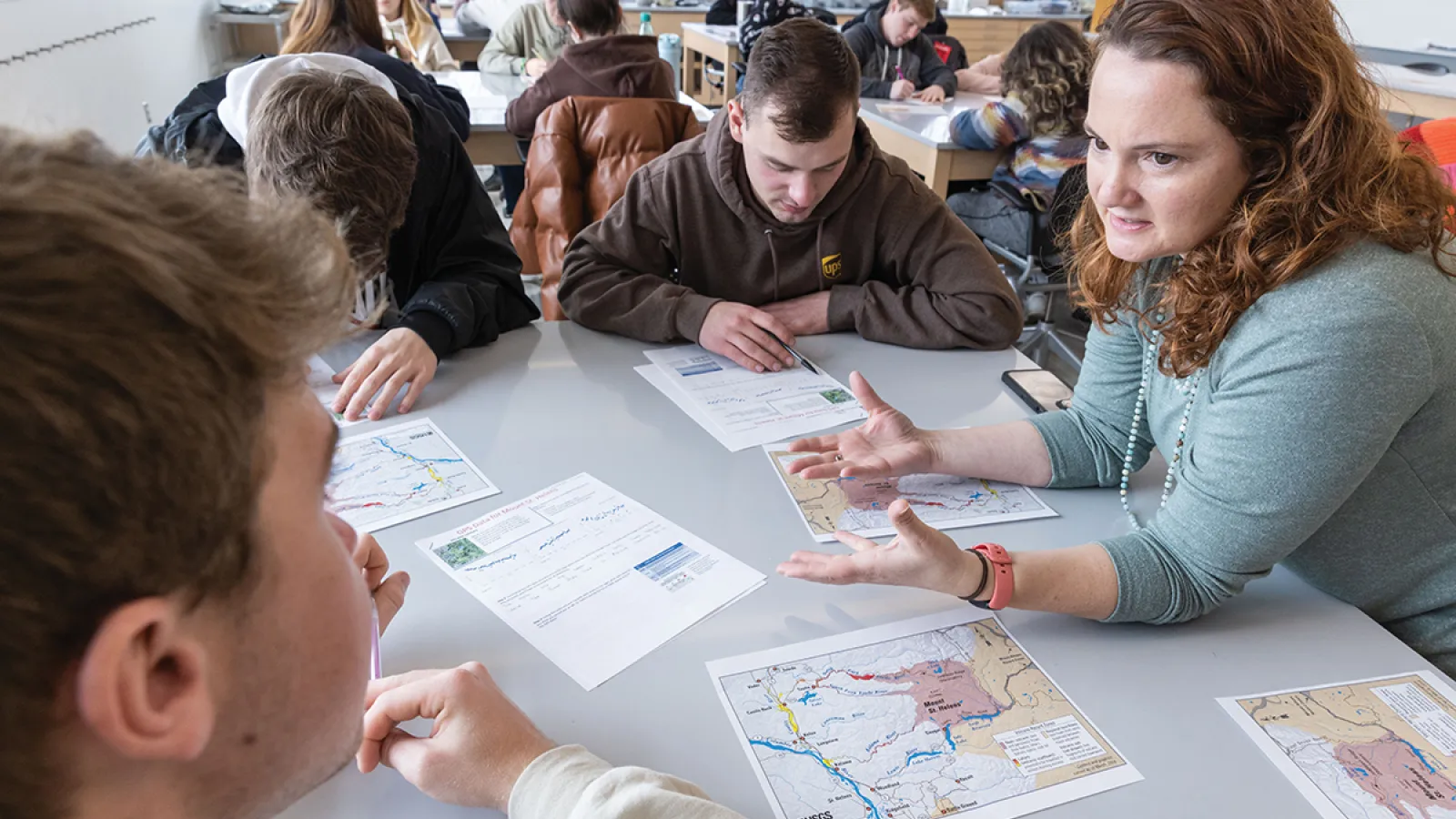 A professor works with a group of students at a table.