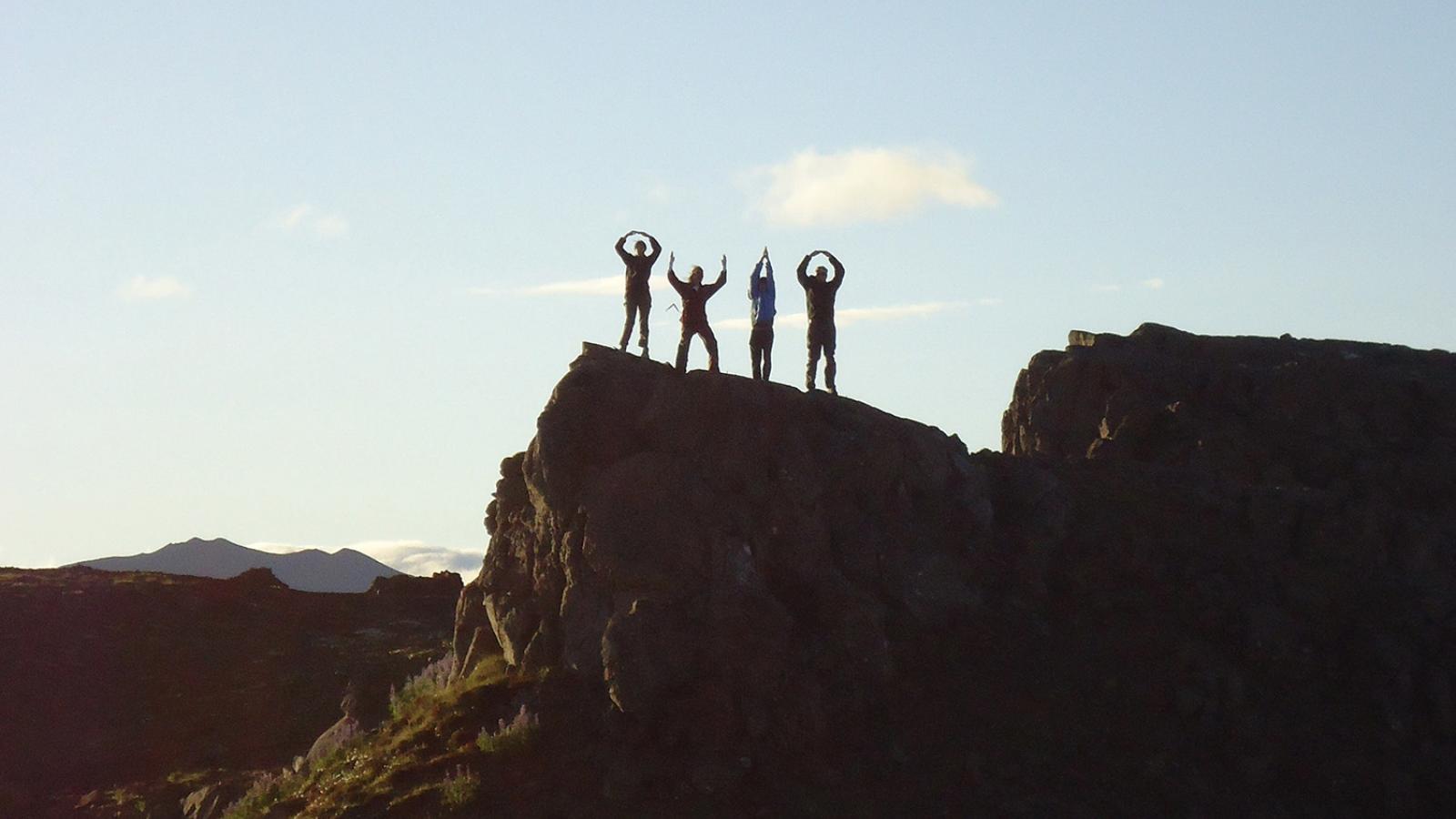 A group of students silhouetted while doing the O-H-I-O pose on top of a cliff