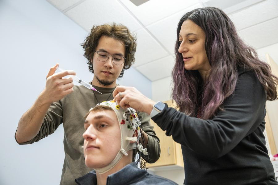 A man and a woman examine a seated man in an EEG electrode cap.