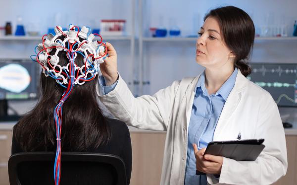 Doctor in white coat attaches electrodes to the head of a patient in a lab.