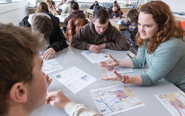 A professor works with a group of students at a table.