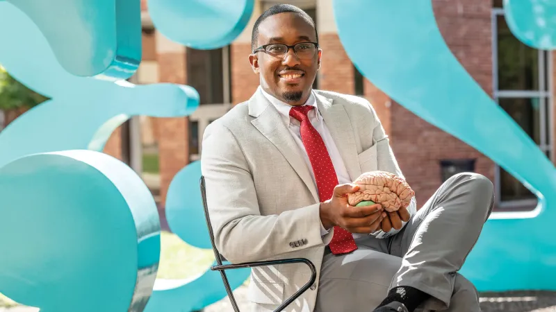 Jeremy Grant holds a model of a human brain while seated in the Garden of Constants