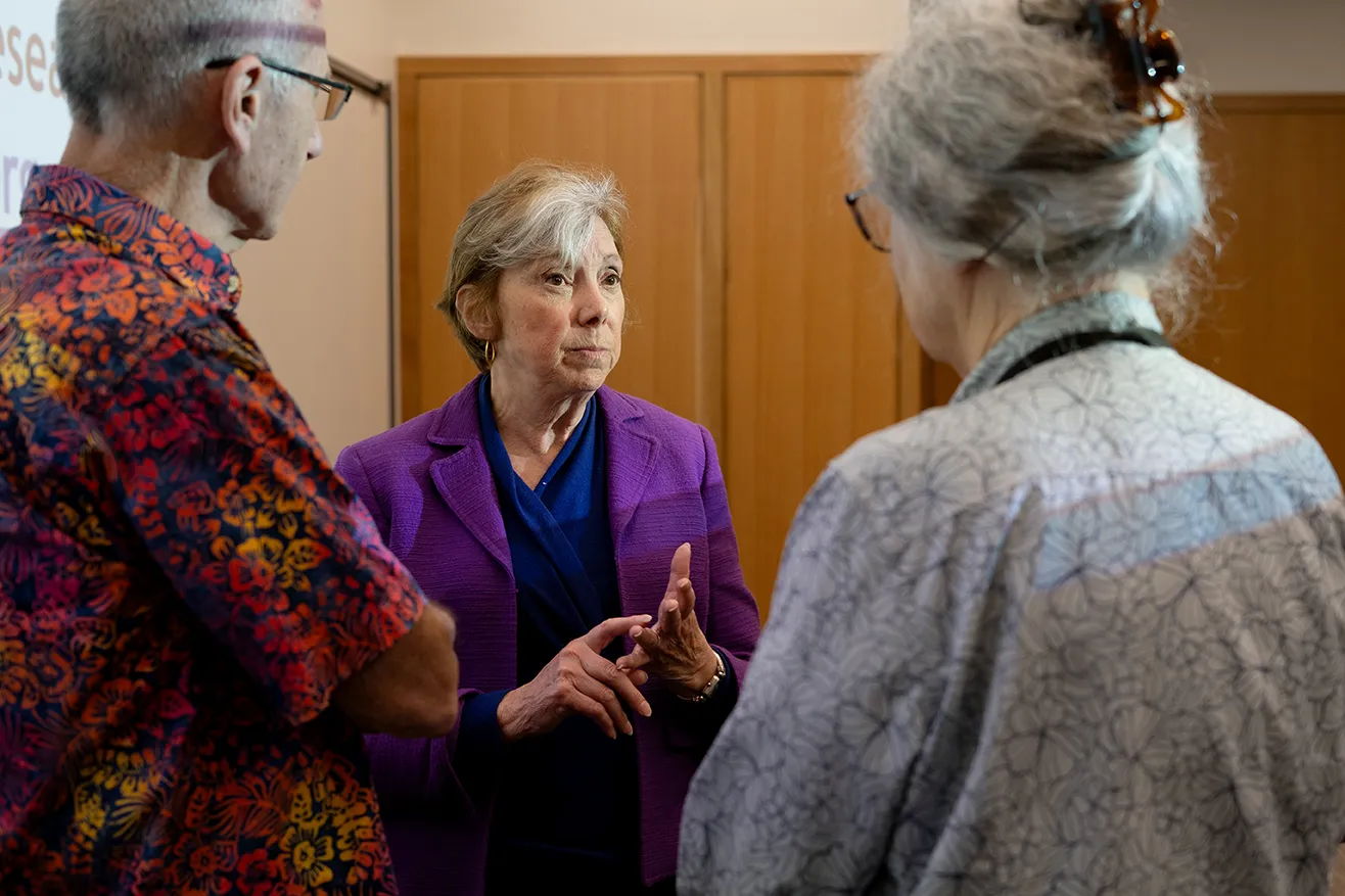 Woman speaks to two people in a lecture hall.